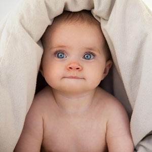 baby peering out from under a down comforter